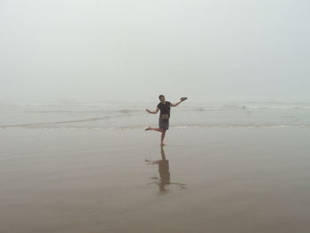 Full length of woman dancing on sea shore at beach against sky during foggy weather