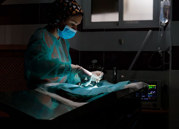 Side view of female veterinarian in uniform and gloves using tools and performing surgery on animal in modern clinic