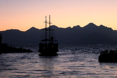 Silhouette sailboat sailing in sea against clear sky during sunset