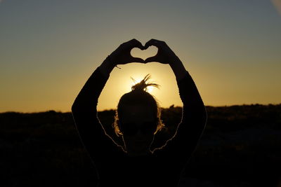 Rear view of silhouette woman heart shape against sky during sunset