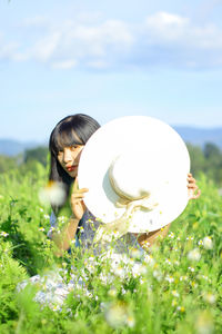 Side view of young woman holding a hat agains flowers 
