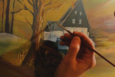 Cropped hand of woman drawing on canvas in cottage