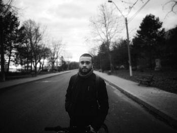 Portrait of young man standing on road against trees