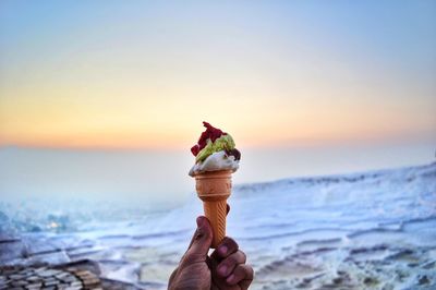 Hand holding ice cream at sunset