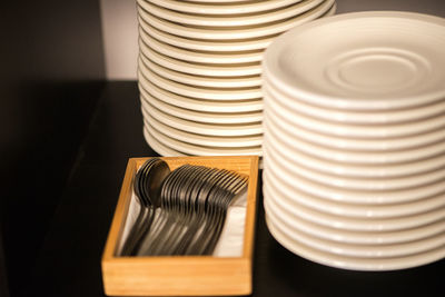 High angle view of plate stacks by spoons in wooden container on table