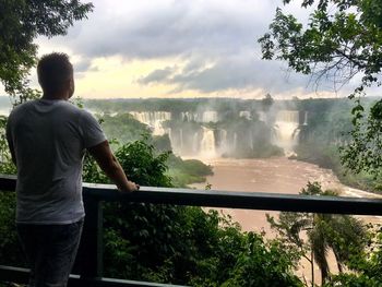 Rear view of man looking at waterfall against sky