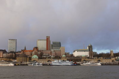 Buildings by river against sky in city