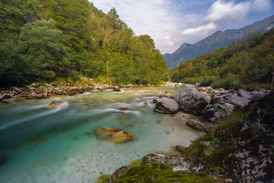 Stream flowing through rocks by river against sky