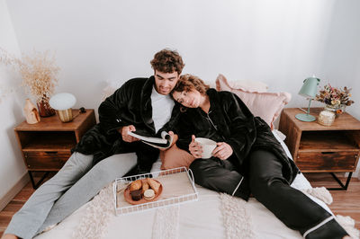 High angle of gentle couple relaxing on bed together while having breakfast in morning