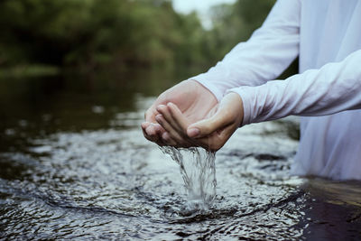 Midsection of woman standing with hands cupped in lake