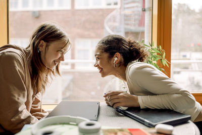 Smiling female teenage friends gossiping with each other at high school