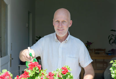 Portrait of smiling man watering flowers at home
