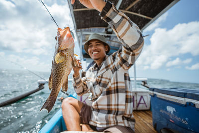 Rear view of man holding fish at beach