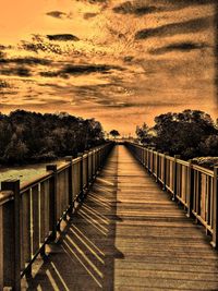 Footpath by railing against sky during sunset