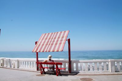 Rear view of woman sitting on bench at promenade against clear blue sky