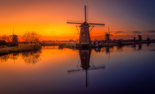 Traditional windmill reflecting on lake against sky at sunset