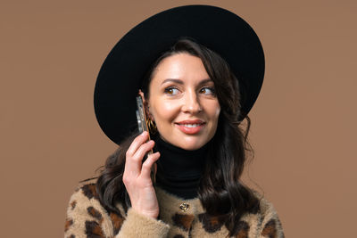 Portrait of woman wearing hat standing against yellow background