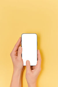 Cropped hands using smart phone against yellow background