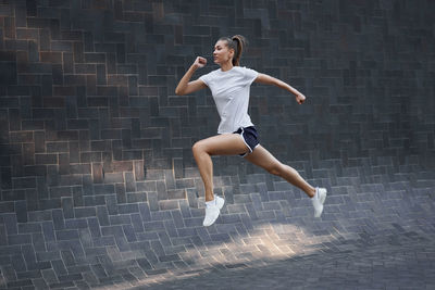 Full length of woman jumping against wall