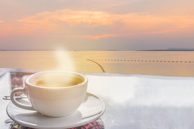 Coffee cup on table against sea during sunset