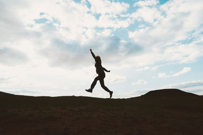 Silhouette mature man jumping on mountain against cloudy sky during sunset