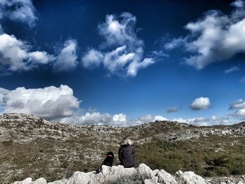 Rear view of woman sitting with dog on mountain against sky