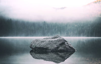 Rock amidst lake during foggy weather