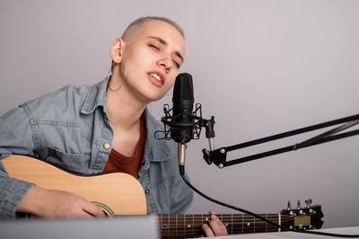Woman singing while playing guitar against gray background