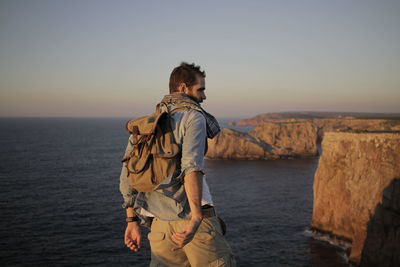 Rear view of man wearing backpack while standing at beach against clear sky