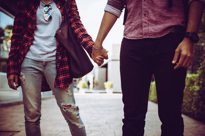 Midsection of couple holding hands on street in city