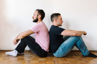 Gay couple sitting back-to-back at home.