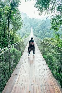 A person wearing a robe standing on a suspension bridge in a tropical rain forest