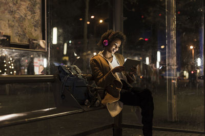 Young woman with headphones and tablet waiting at the tram stop