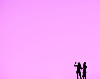 Silhouette man and woman standing against pink sky