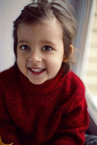 Boy child in red knitted sweater and hat sitting on the window in autumn