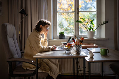 Side view of young woman sitting at home