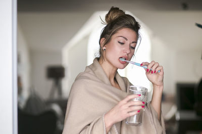 Young woman brushing teeth while holding glass of water