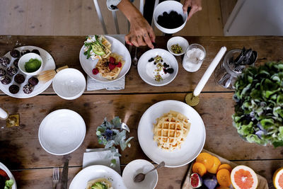 Woman adding blackberries in cream on plate by vase at wooden table