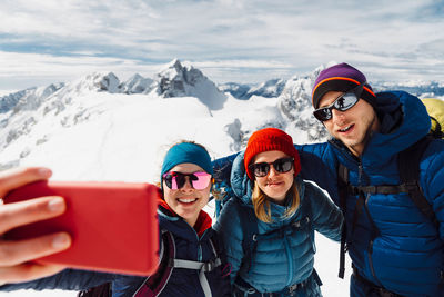 Portrait of smiling friends sitting on snowcapped mountain