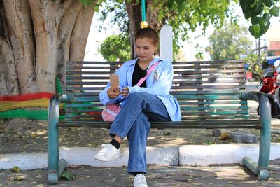 Full length of young woman using smart phone while sitting on bench