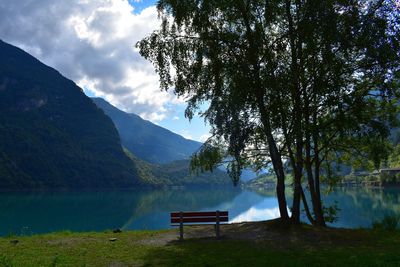 Bench in park by lake against sky