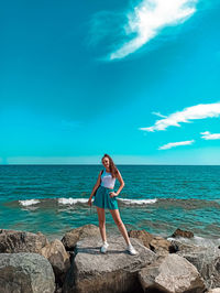 Woman standing on rock by sea against blue sky