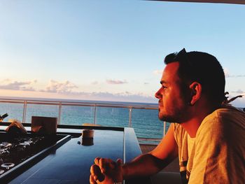 Man sitting at table by sea against sky