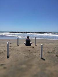 Rear view of man sitting on beach against clear sky