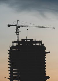 Silhouette of tower cranes in operation at construction site with during sunset.
