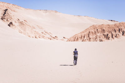 Man walking on sand dune in desert against clear sky