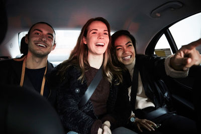 Happy woman pointing and showing to friends while sitting in car