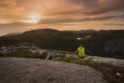 Rear view of man sitting on cliff against sky