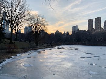 Scenic view of frozen river by buildings against sky during sunset