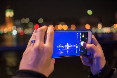 Cropped image of woman photographing illuminated city through smart phone